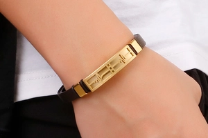 Detail view of gold heartbeat plaque on dark brown textured wristband on wrist