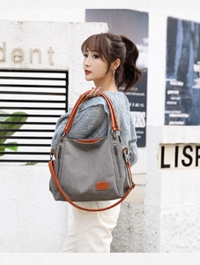 Detail of grey canvas tote bag featuring brown leather straps and a vintage logo patch