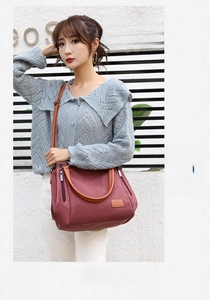 Detail view of burgundy canvas shoulder bag with brown straps and functional zip pocket