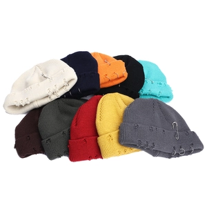 Flat lay display of colorful distressed knit beanies with metal rings and pins detail