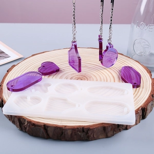 Siliconen mal voor hars hangers met paarse harsstukken op een houten basis in glas