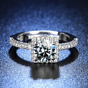 Close-up of a silver ring with round center diamond and square halo on a blue surface