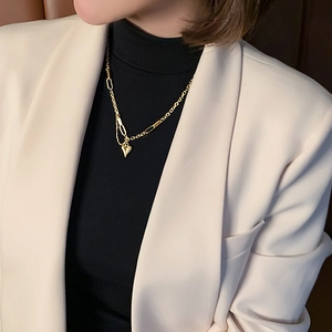Détail d'un collier cœur doré porté avec un blazer chic et un col roulé noir élégant