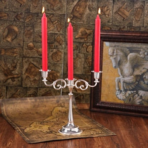 Vintage silver 3-arm metal candelabra with red candles on a dark wooden table background