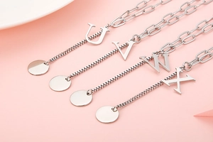 Detail of four silver letter pendants U V W X on polished chains over pink background