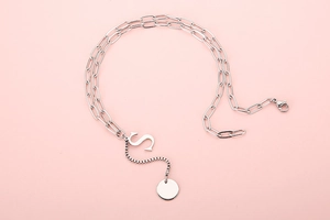 Detail of silver paperclip chain necklace with capital letter S and round metal pendant