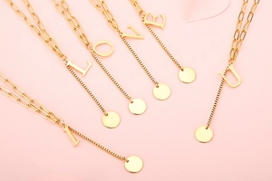 Detail of gold double-layered necklace featuring letter pendants and round metal charms