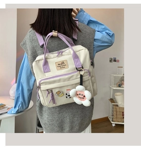 Detail of white canvas crossbody bag with purple straps and cute plush flower pendant