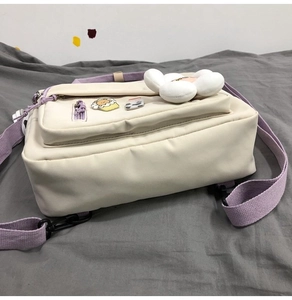 Close-up of canvas bag with purple strap, white plush flower and cute cartoon badges