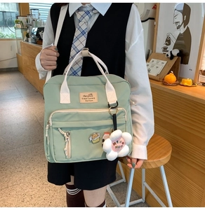 Light green canvas tote bag with floral plush charm and white adjustable straps in cafe setting