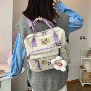 Detail of cream canvas backpack with purple straps and cute plush flower keychain charm