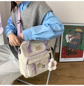 Detail of canvas messenger bag in off-white with purple straps and floral plush pendant