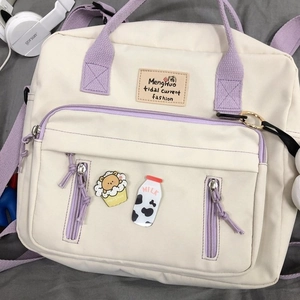 Detail of canvas backpack in beige and purple showing front zipper pockets and cute brooches