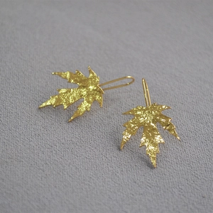 Macro view of gold maple leaf earrings with hammered texture on gray fabric