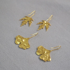 Golden maple and ginkgo leaf earrings with hammered metal texture on grey base