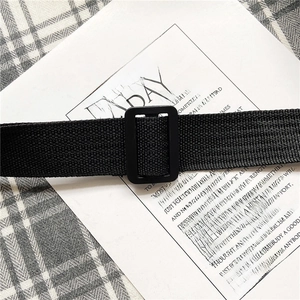 Detail shot of black canvas belt featuring a matte square buckle on a textured background