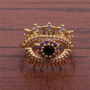 Golden evil eye ring with purple and black zircon crystals on a wooden background