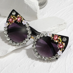Cat eye sunglasses with rhinestones and floral accents on a white decorative stone