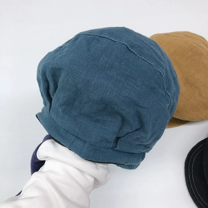 Presentazione a mano di un berretto newsboy blu in cotone e lino con cuciture bianche