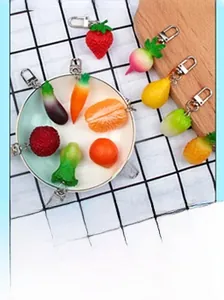 Detailed overhead view of assorted PVC fruit and vegetable keychains on a white ceramic bowl