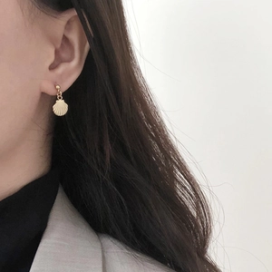 Close-up of a model wearing a 14K gold shell-shaped earring with fine brushed texture