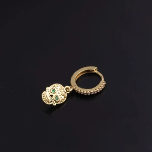 Detail of gold skull earring featuring green gemstone eyes and micro-pave crystals