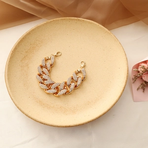 Vista dettagliata di un bracciale a catena cubana dorata con cristalli su un piatto di ceramica