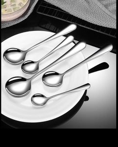Set of six stainless steel spoons in various sizes on a white plate over a black surface