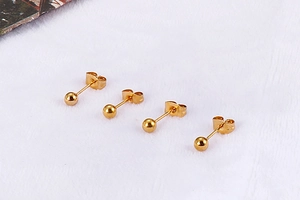 Close-up of four golden spherical stud earrings with butterfly backs on white plush fabric