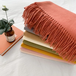 Stack of colorful solid cashmere-like scarves with tassels in soft home setting
