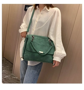 Dettaglio della borsa Boston verde scuro opaca con catena indossata da una modella in interno
