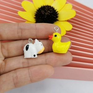 Miniature resin cow and yellow duck charms held by hand for DIY jewelry making