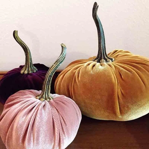 Three velvet decorative pumpkins in purple, pink, and yellow with resin stems on wood