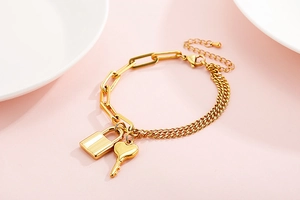 Close-up of gold chain bracelet with key and padlock charms on a soft pink background