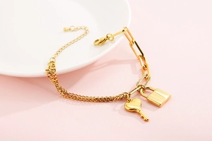 Detail of gold chain bracelet with irregular links, padlock pendant, and small key charm