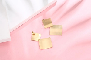 Detail of gold geometric square stud earrings with brushed metallic texture finish