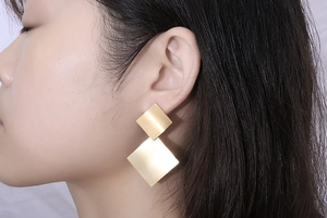 Detailed close-up of large geometric gold earrings with a brushed metallic texture