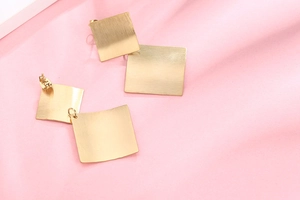 Detail of geometric square gold earrings with a brushed metal texture on pink silk fabric