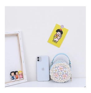 Mini round tweed bag with 3D flowers shown next to a smartphone for size reference