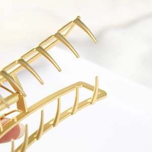 Macro detail of matte gold rectangular hair claw clip showing strong spring and teeth