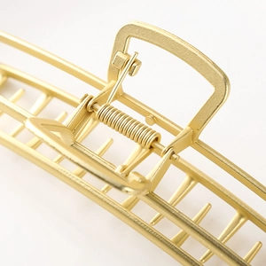 Macro detail of a large matte gold metal hair claw clip with spring and grip teeth