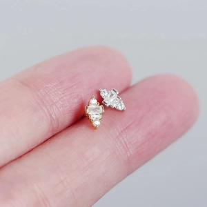 Macro view of gold and silver mini geometric stud earrings held on a fingertip