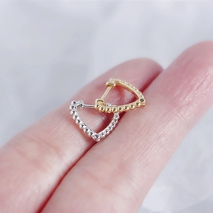 Macro shot of silver and gold heart earrings with bead texture on fingertips