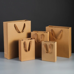 Vertical kraft paper gift bags in five sizes with durable woven handles on grey background