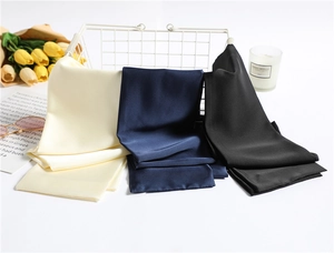 Detailed close-up of folded silk-satin scarves in beige, navy blue, and black colors