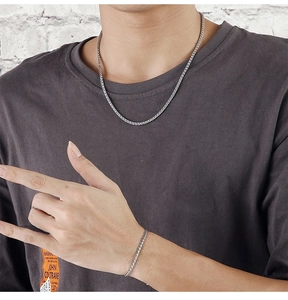 Close-up of a silver woven chain necklace and bracelet set worn by a male model