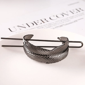 Macro detail of elegant black metal feather hair pin with fine textures on a white tray