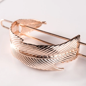 Elegant rose gold metal feather hair pin for women with detailed texture on pink surface
