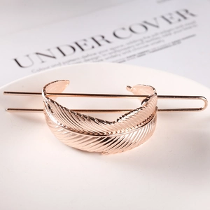Detail view of a rose gold feather-shaped hair pin with metal texture on a white tray