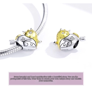 Macro detail of S925 silver heart charm with Cupid arrow and gold-plated scrollwork